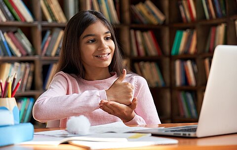 Barrierefreiheit für Schulen und Schulträger Ein Mädchen sitzt vor einem Laptop und spricht Gebärdensprache vor der Laptop-Kamera.
