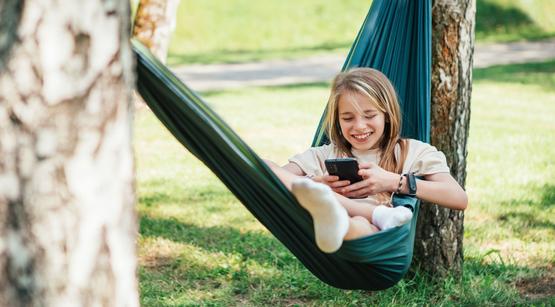 Spotlight Medienzeit trifft Ferienzeit Teenager-Mädchen liegt im Garten in einer Hängematte und schaut auf ihr Handy