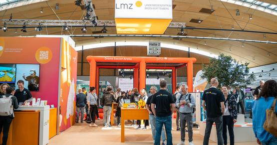 LMZ-Stand und Drohnen-Parcours auf der Learntec Messebesuchende und LMZ-Mitarbeitende auf dem orangeroten LMZ-Messestand auf der Learntec.