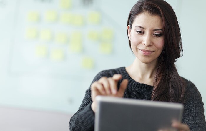 Junge Frau mit Tablet in den Händen vor einer Pinnwand Junge Frau mit Tablet in den Händen vor einer Pinnwand