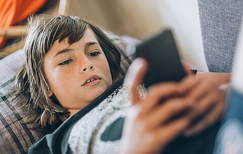 Junge schaut auf sein Smartphone Junge liegt auf dem Smartphone und schaut sich sorgenvoll etwas auf seinem Smartphone an.