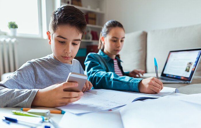 Zwei Kinder am Schreibtisch mit Handy und Laptop Zwei Kinder am Schreibtisch mit Handy und Laptop