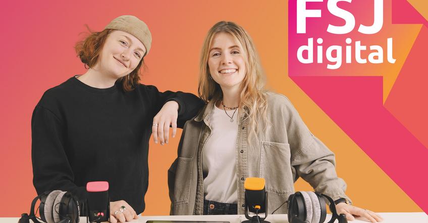 FSJ digital Zwei junge Frauen stehen lächelnd vor einem Tisch mit zwei Mikrofonen, Kopfhörern und einem Tablet.