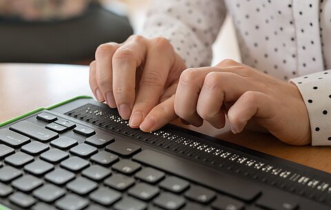 Barrierefreie Websites Die Hände einer Frau liegen einer Computertastatur mit Braillezeile und geben etwas in Brailleschrift ein.
