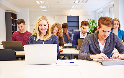 Jugendliche vor ihren Laptops in einer Schulklasse.