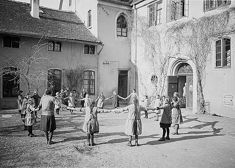 Denkendorf: Volkshochschule, Kinderreigen 1930, Robert Bothner Schulmädchen im Pausenhof mit Lehrerin im Kreis an einem sonnigen Wintertag.