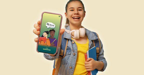 Tool-Tipp RE:think Ein Mädchen in gelbem T-Shirt mit Jeansjacke und hellrosa Kopfhörern um den Hals hält ein Handy in die Kamera, auf dem das Startbild der App RE:think zu sehen ist.