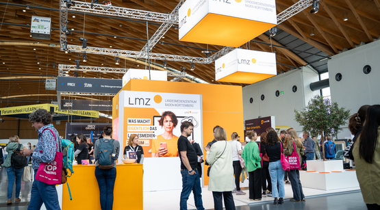 Messestand des LMZ in leuchtendem Orange, davor eine Menschenmenge