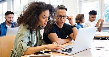 Eine Schülerin und ein Schüler schauen gemeinsam in einen Laptop.