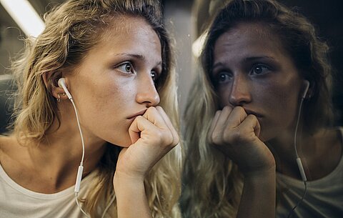 Opfer von sexueller Belästigung nachdenklich in der U-Bahn Ein Mädchen mit lockigen Haaren und Kopfhörern hält sich die Hand nachdenklich an den Mund und starrt aus dem Fenster einer U-Bahn, in dem sich ihr Spiegelbild zeigt.