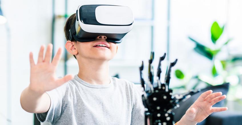 KI Mediendatenbank VR-Brille Ein Junge hat eine VR-Brille auf und hält seine Hände in die Luft. Vor ihm steht eine Roboterhand.